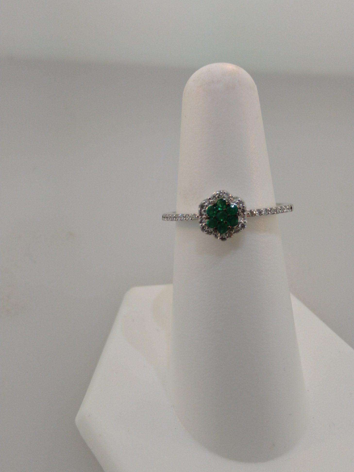 Emerald and diamond ring on a white display stand.