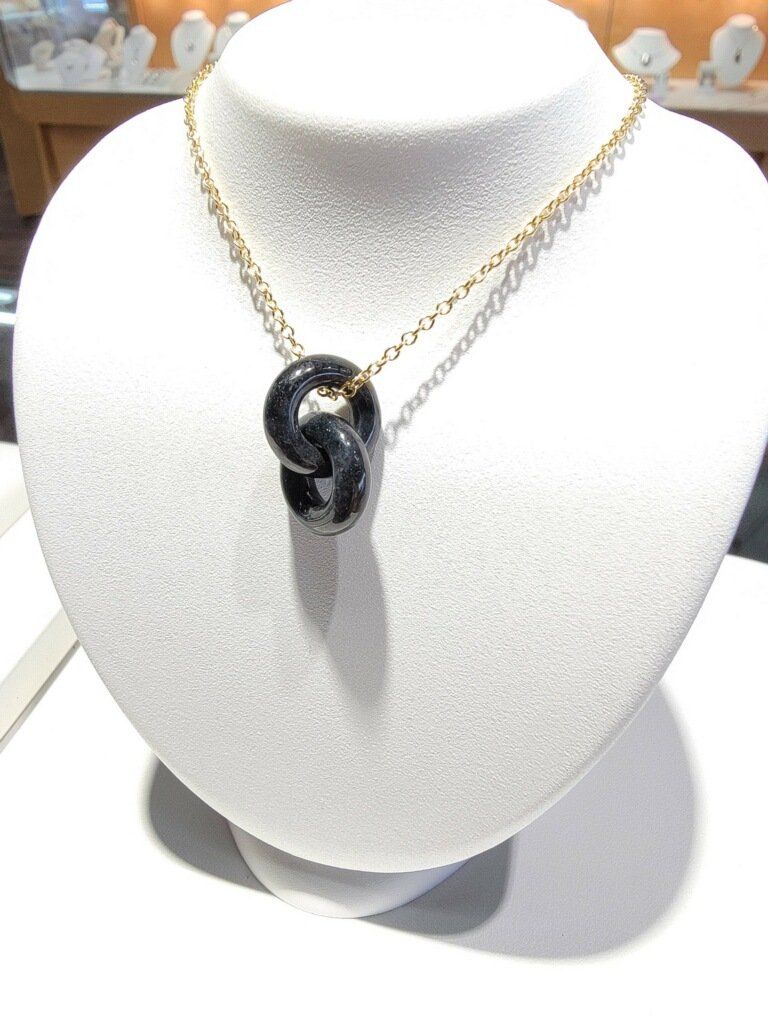 Necklace with a dark pendant shaped like intertwined links on a gold chain, displayed on a white bust.