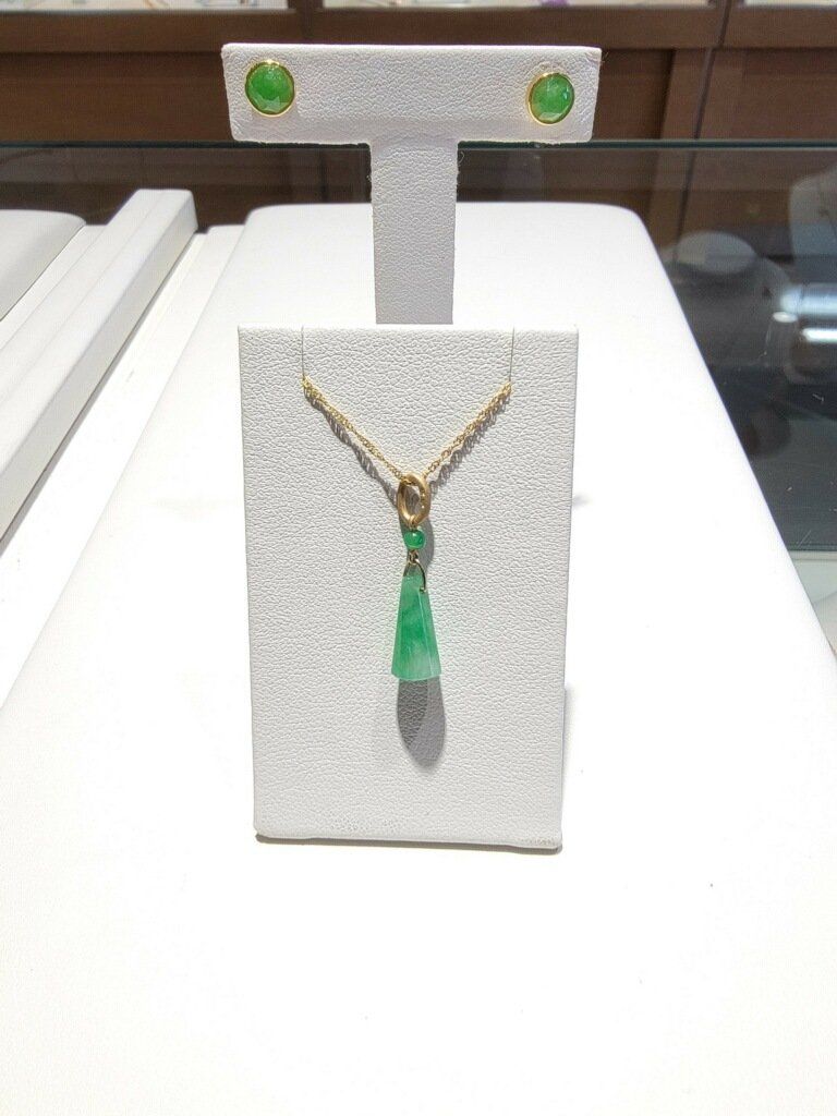 Jade necklace and earrings displayed on a white textured stand in a jewelry store.