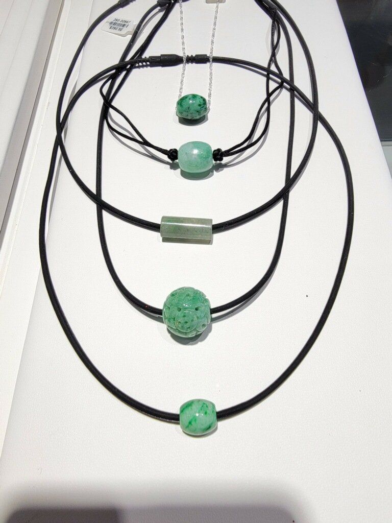 Jade bead necklaces displayed on a white surface, featuring different shapes and black cords.