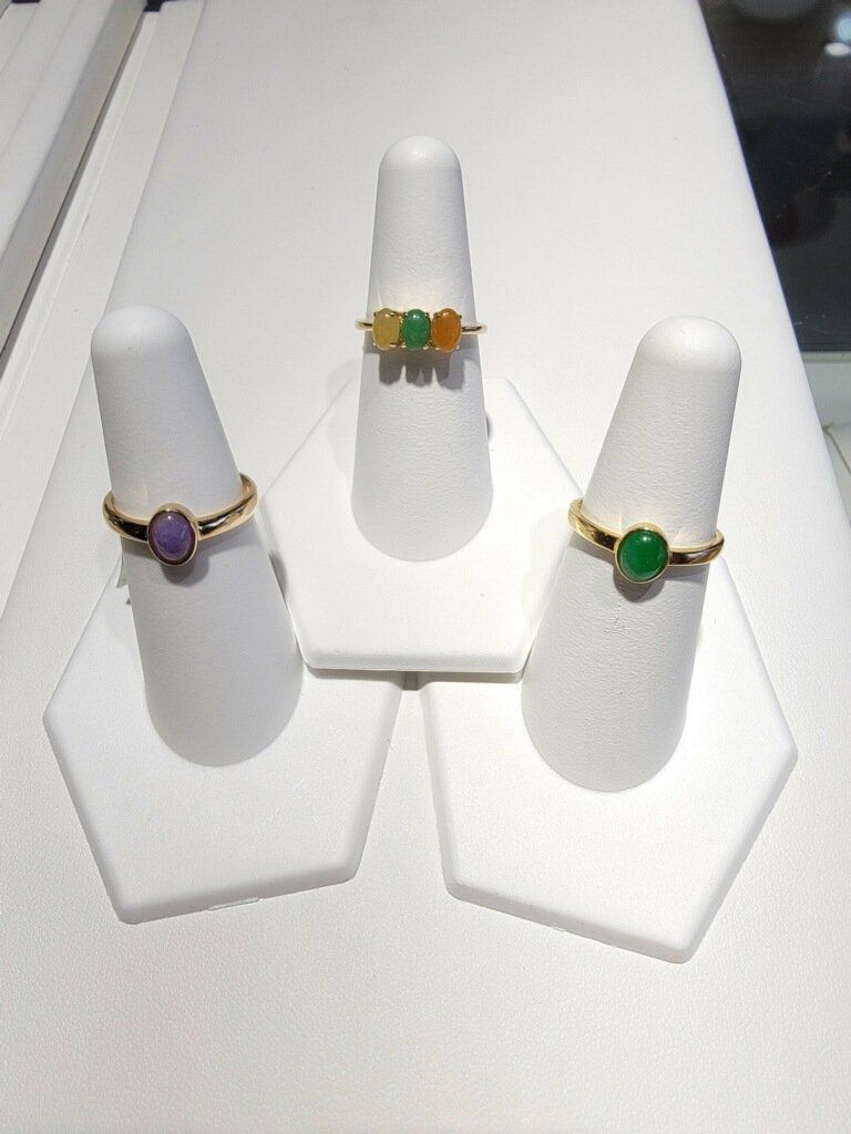 Three gold rings with colorful stones displayed on white stands.