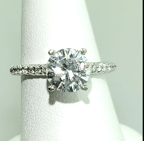 Diamond ring with a large center stone and small stones on the band, set on a white finger form.