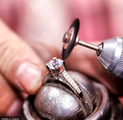Jeweler polishing a diamond ring with a rotary tool in a workshop setting.