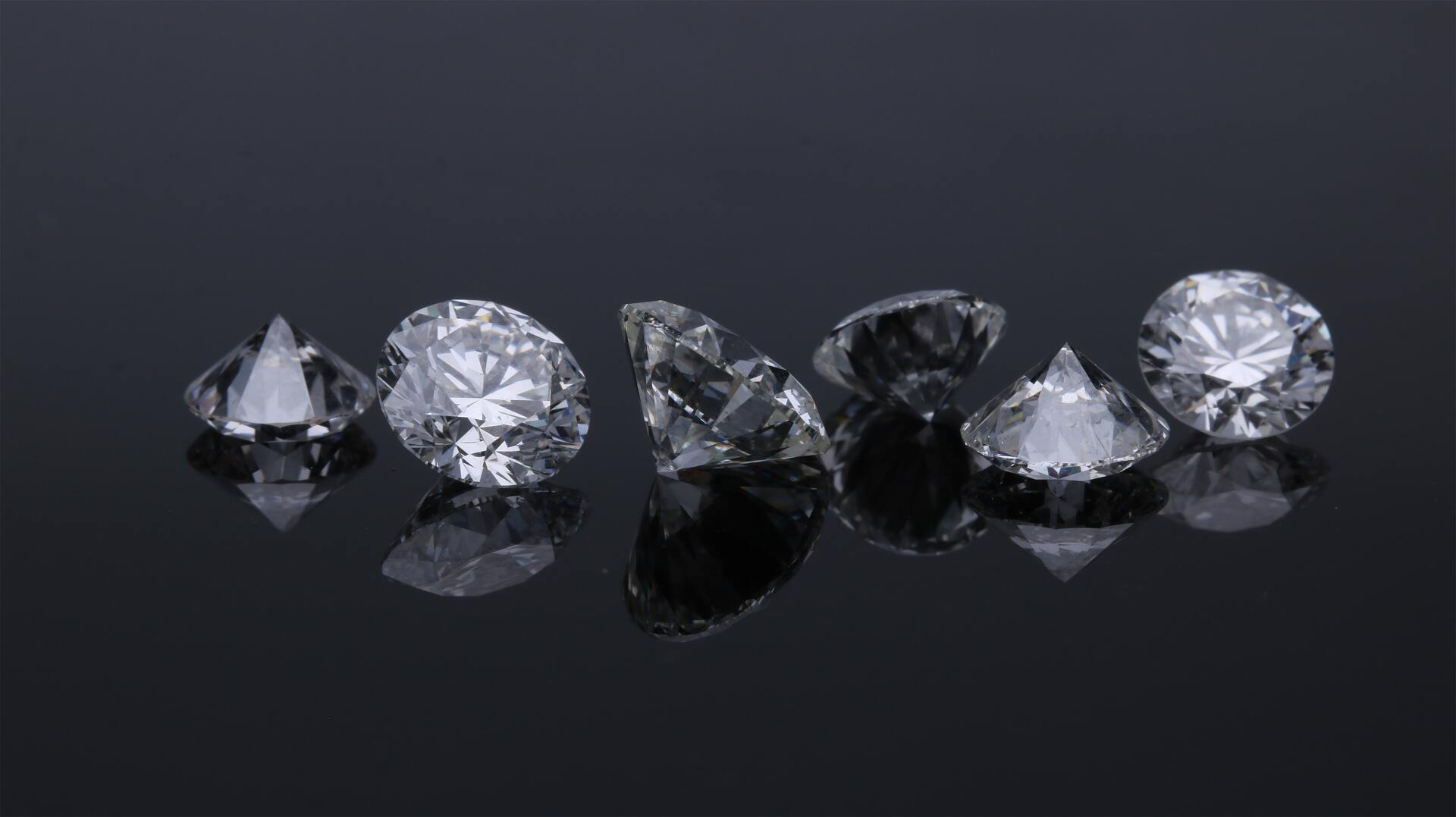 Diamonds on a reflective black surface, showcasing their facets.