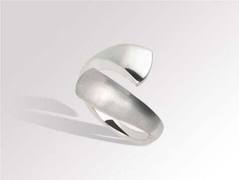 Silver ring with a modern, curved design, resting on a white surface.