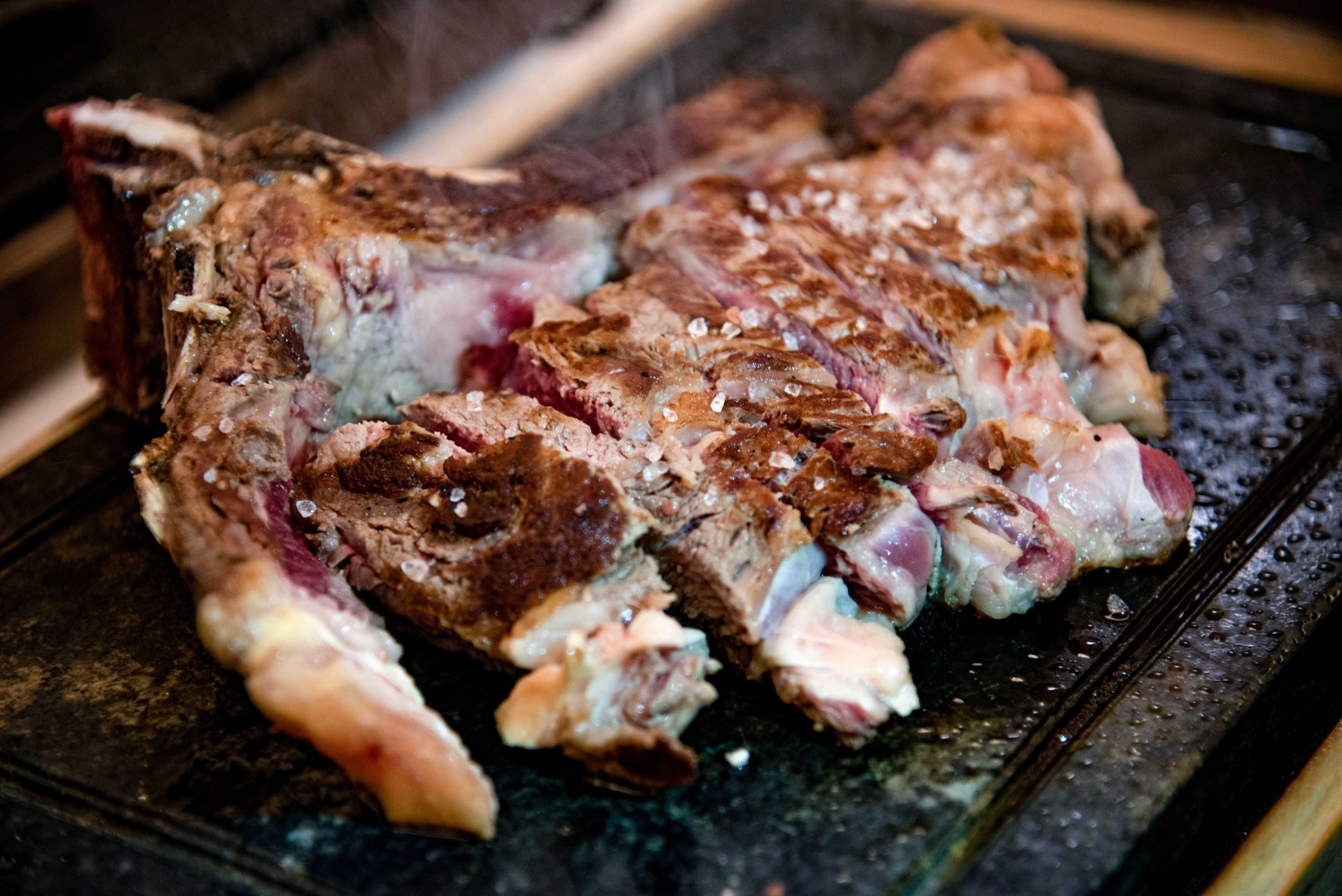 Bistecca tagliata a fette e scottata su una pietra calda; sale cosparso sopra; vapore che sale.