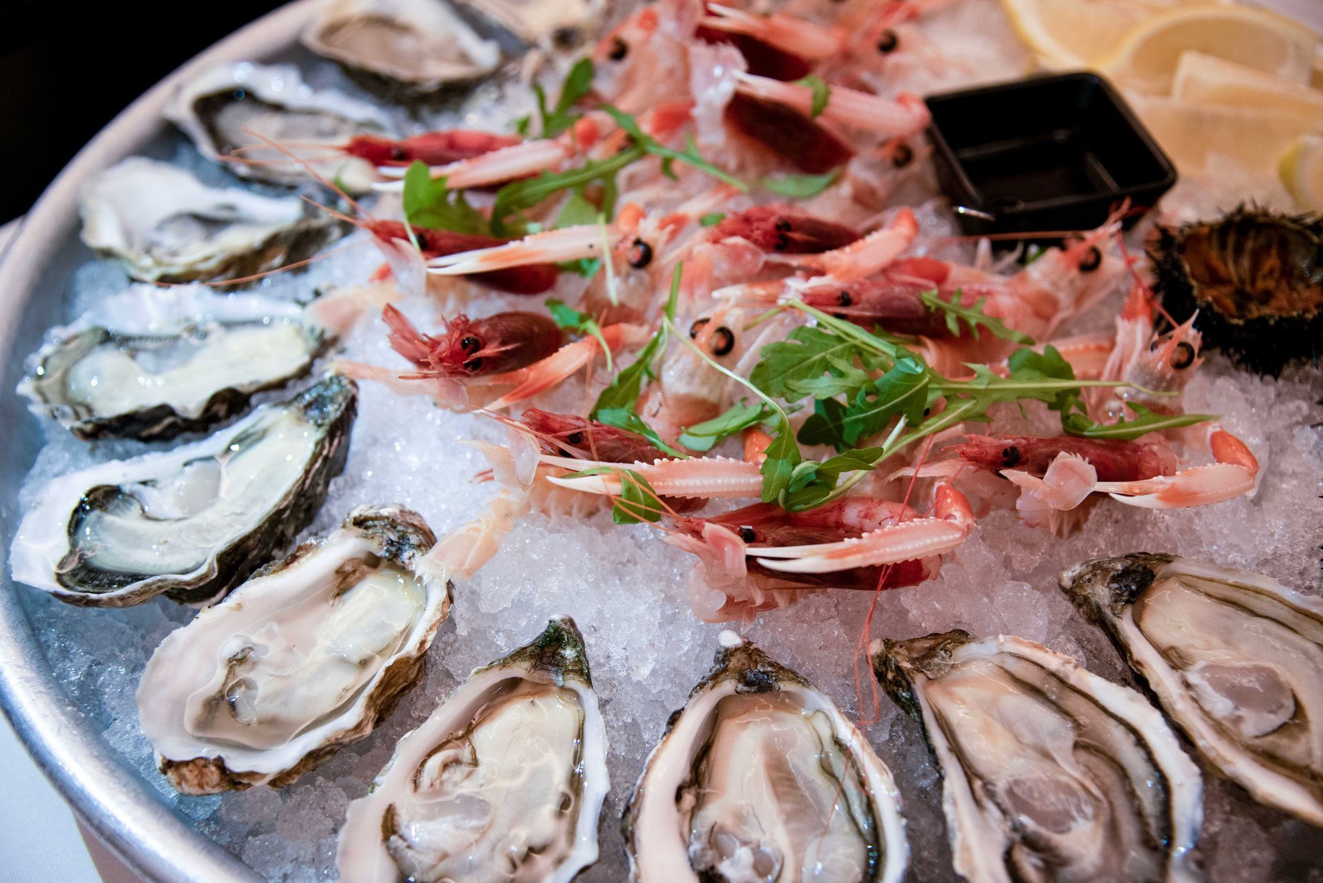 Piatto di frutti di mare su ghiaccio: ostriche, gamberi, fette di limone e un piccolo piatto di salsa.
