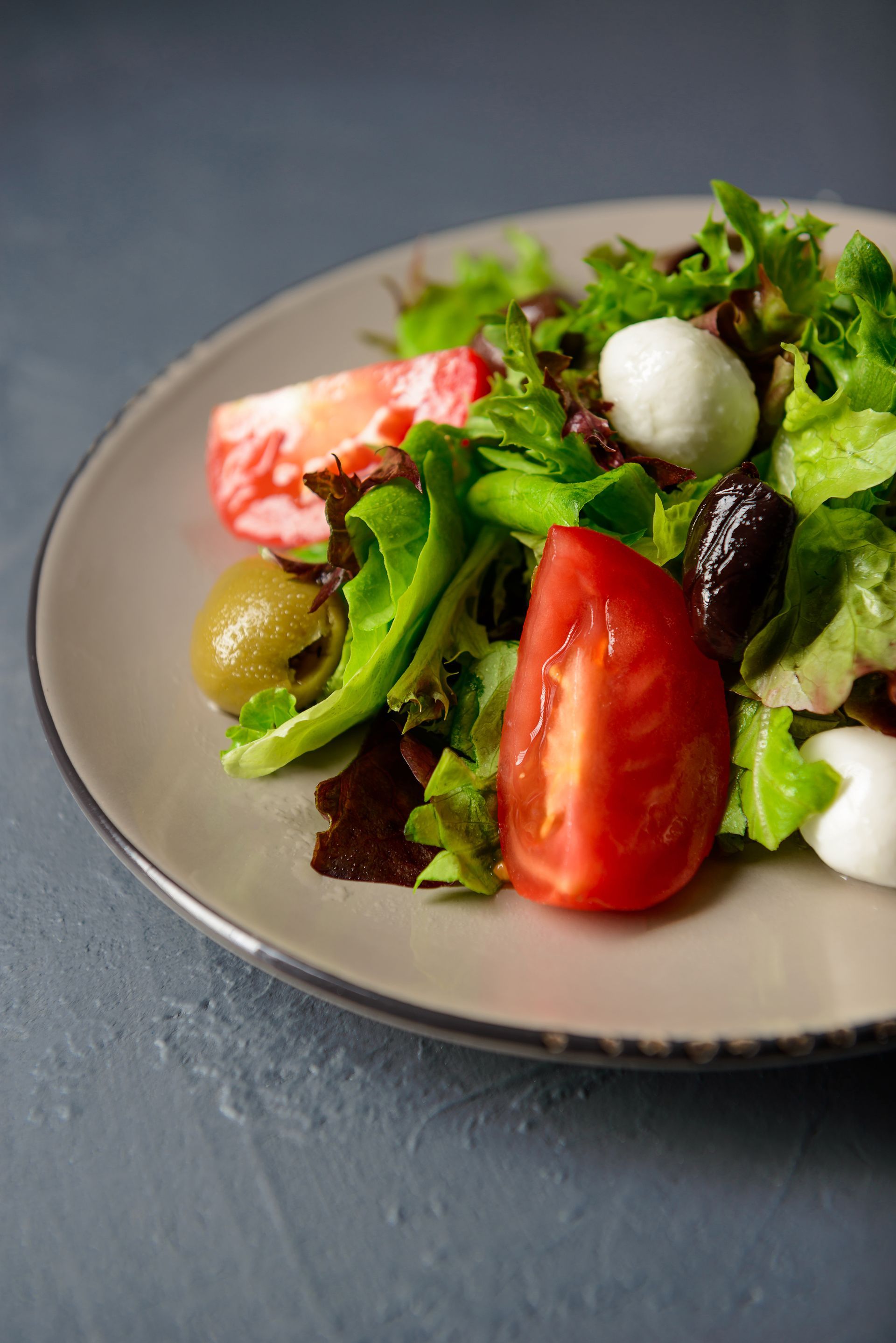 Insalata con lattuga, pomodori, olive e mozzarelline su un piatto grigio.