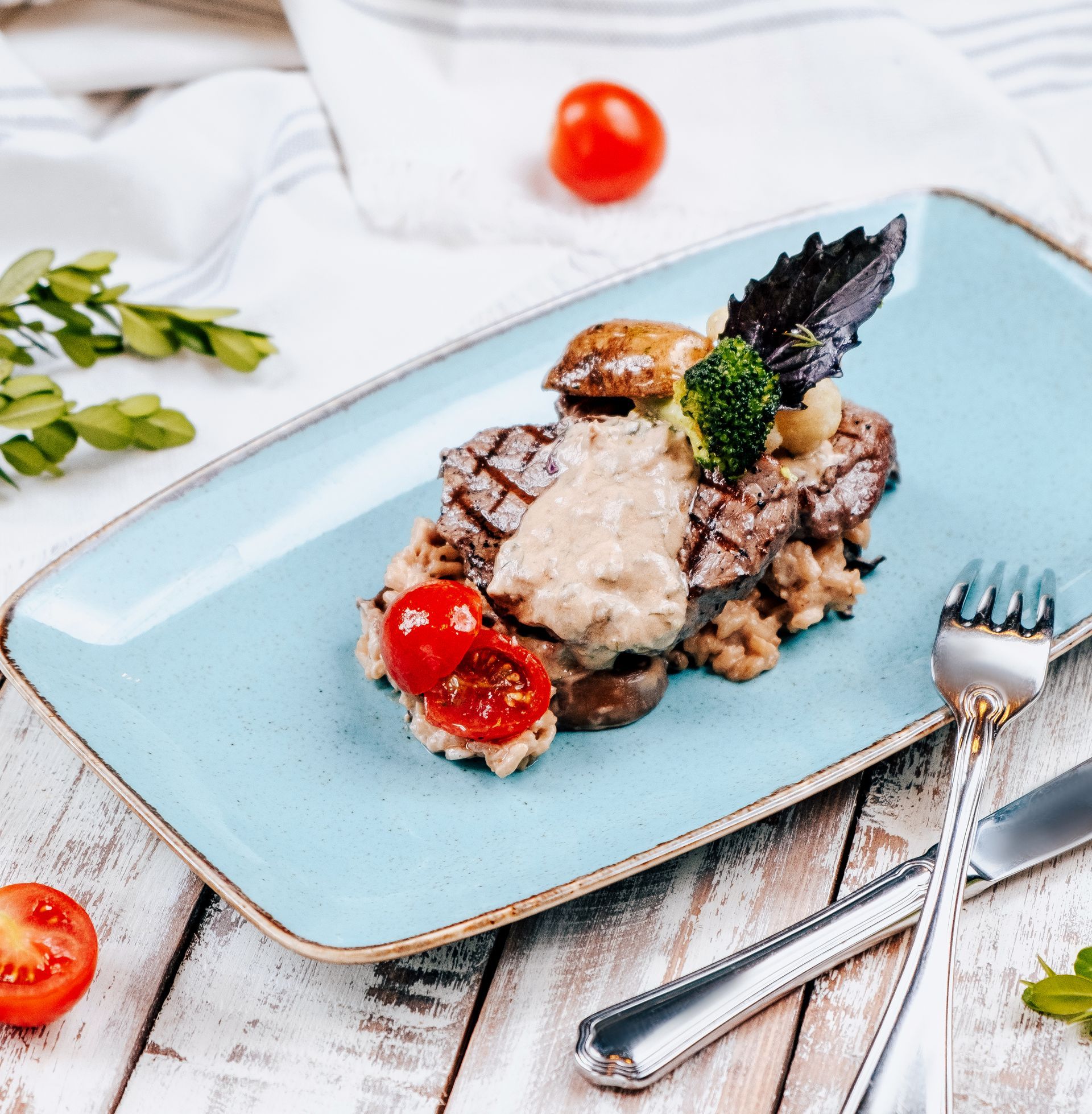 Piatto di bistecca con salsa ai funghi, pomodorini e guarnizione su un piatto blu.
