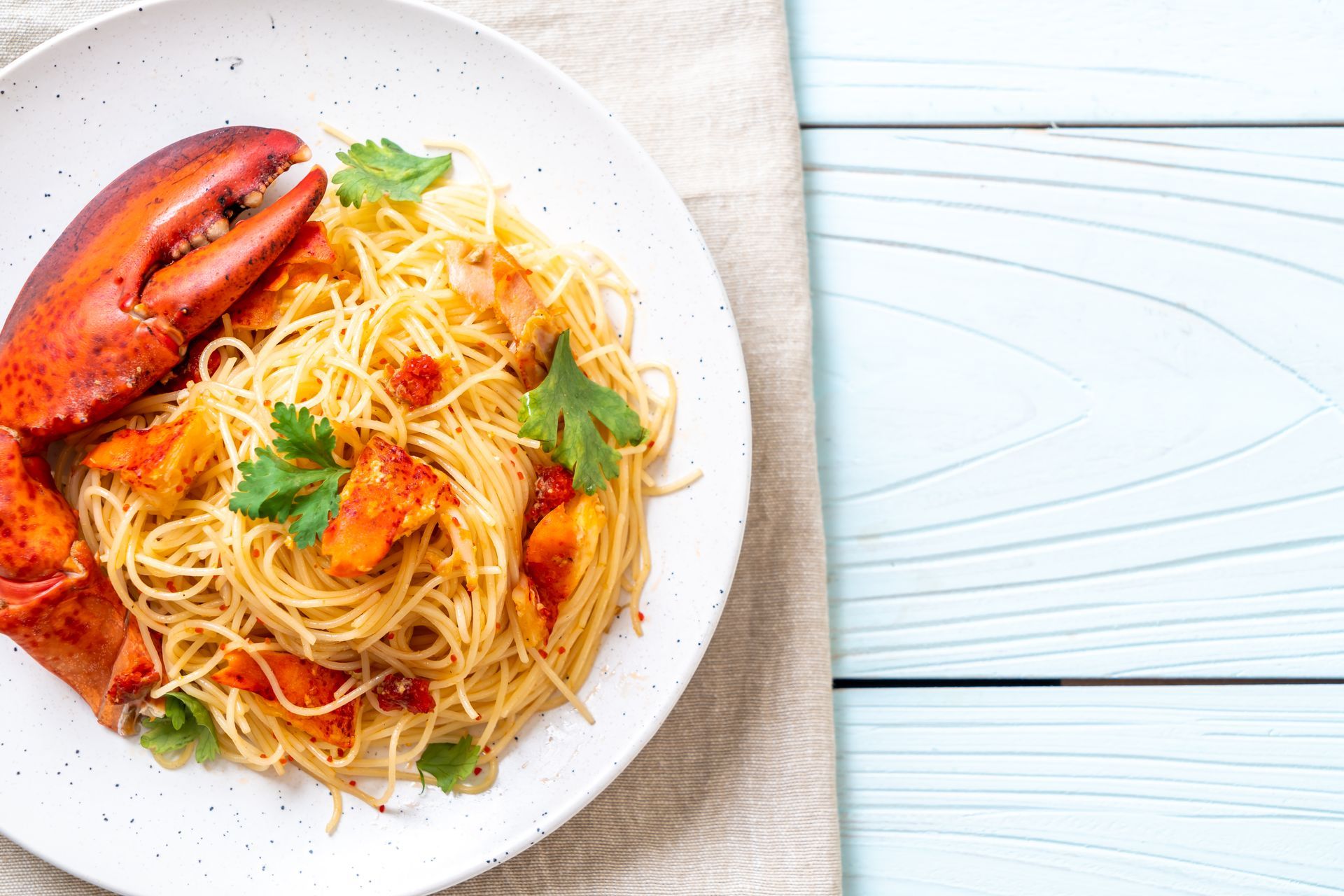 Pasta all'astice su un piatto bianco con prezzemolo fresco, chele di aragosta e sfondo di legno azzurro.