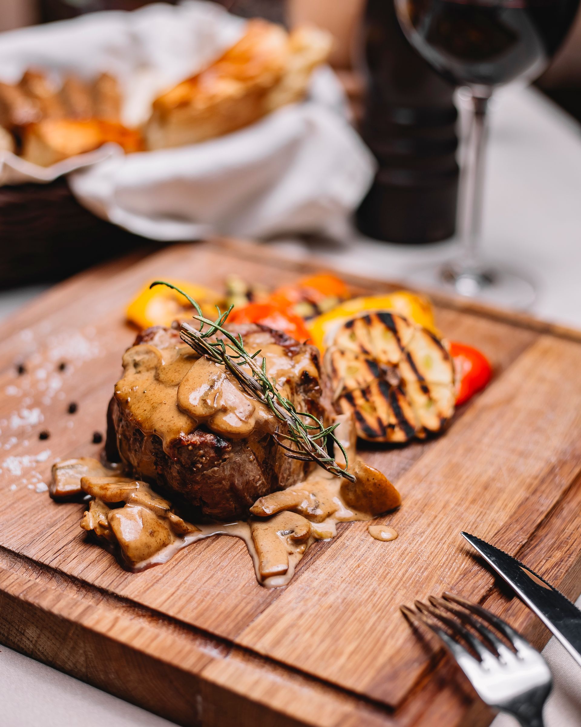 Bistecca con salsa ai funghi, verdure grigliate, rosmarino, su tagliere di legno, con posate.