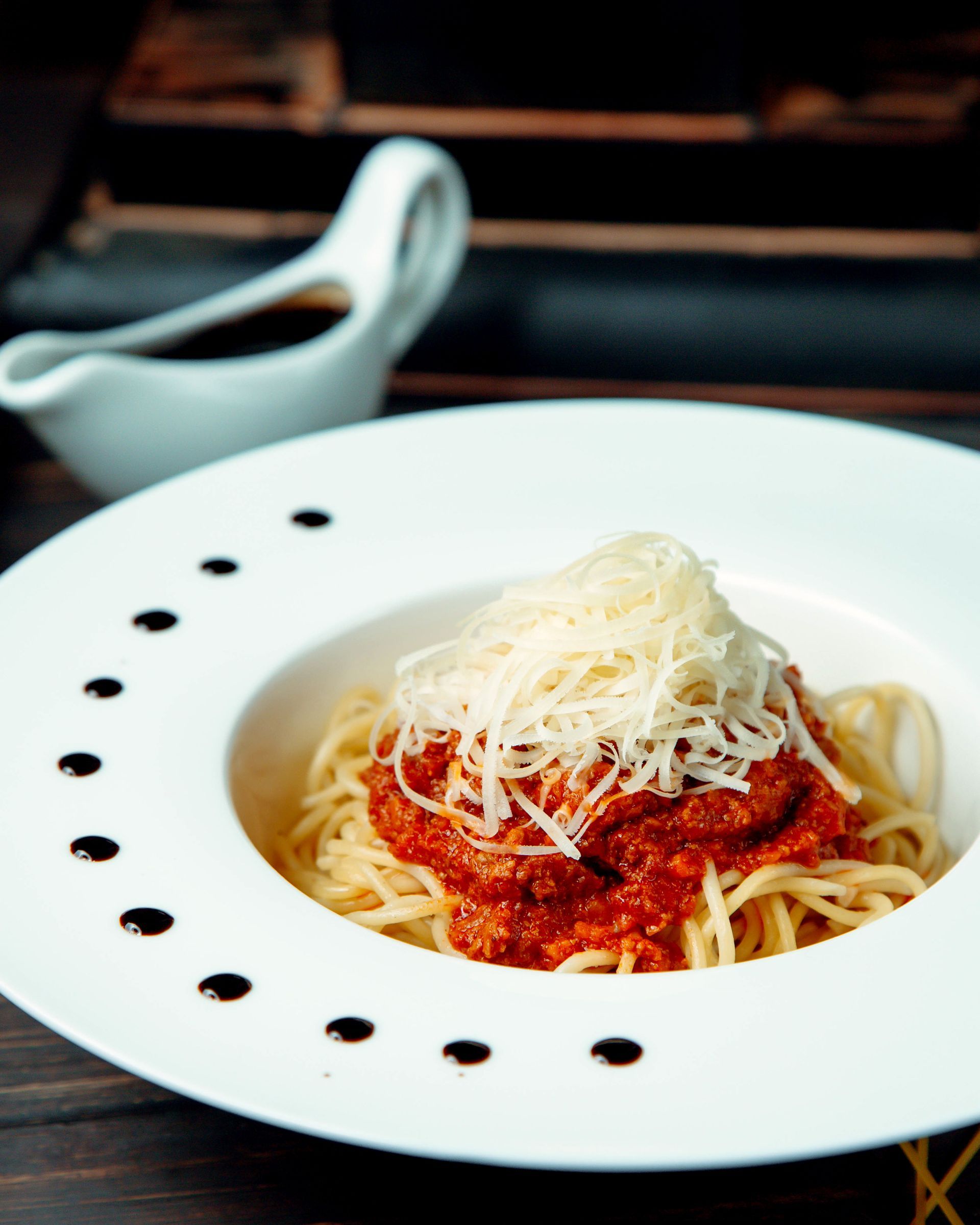 Spaghetti con salsa rossa e formaggio grattugiato in una ciotola bianca, salsiera con salsa scura.