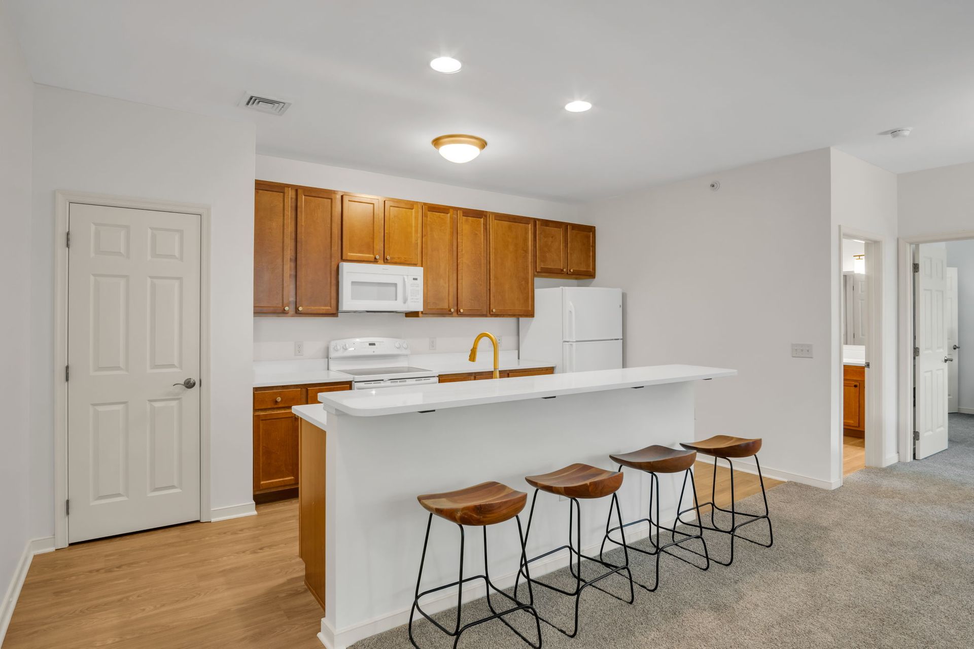 Bright kitchen with white island, wooden cabinets, and four stools in an open living space