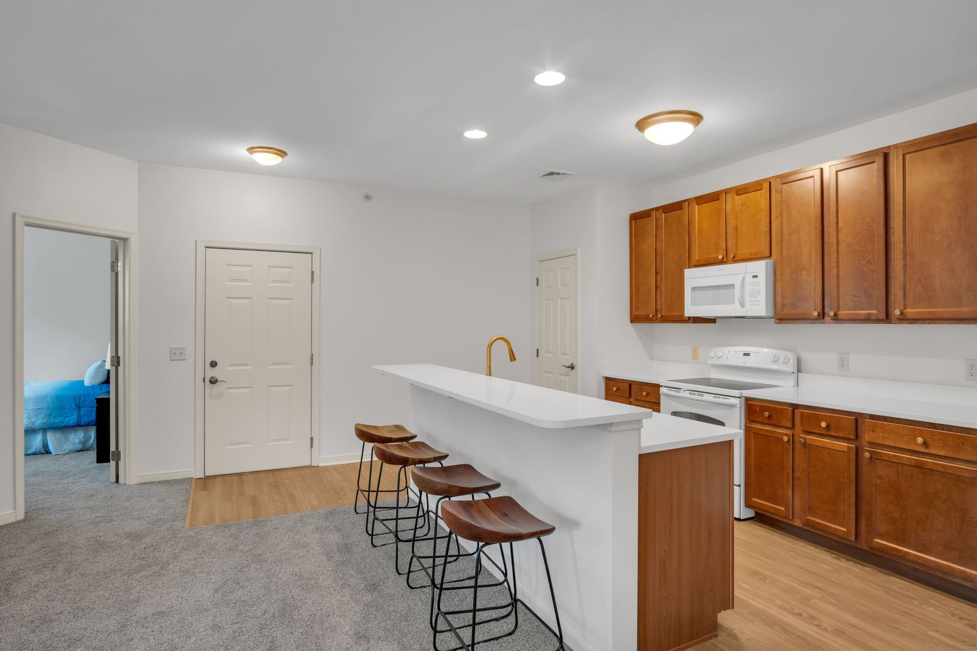 Bright kitchen with white island and stools, wood cabinets, white appliances, and recessed lighting.
