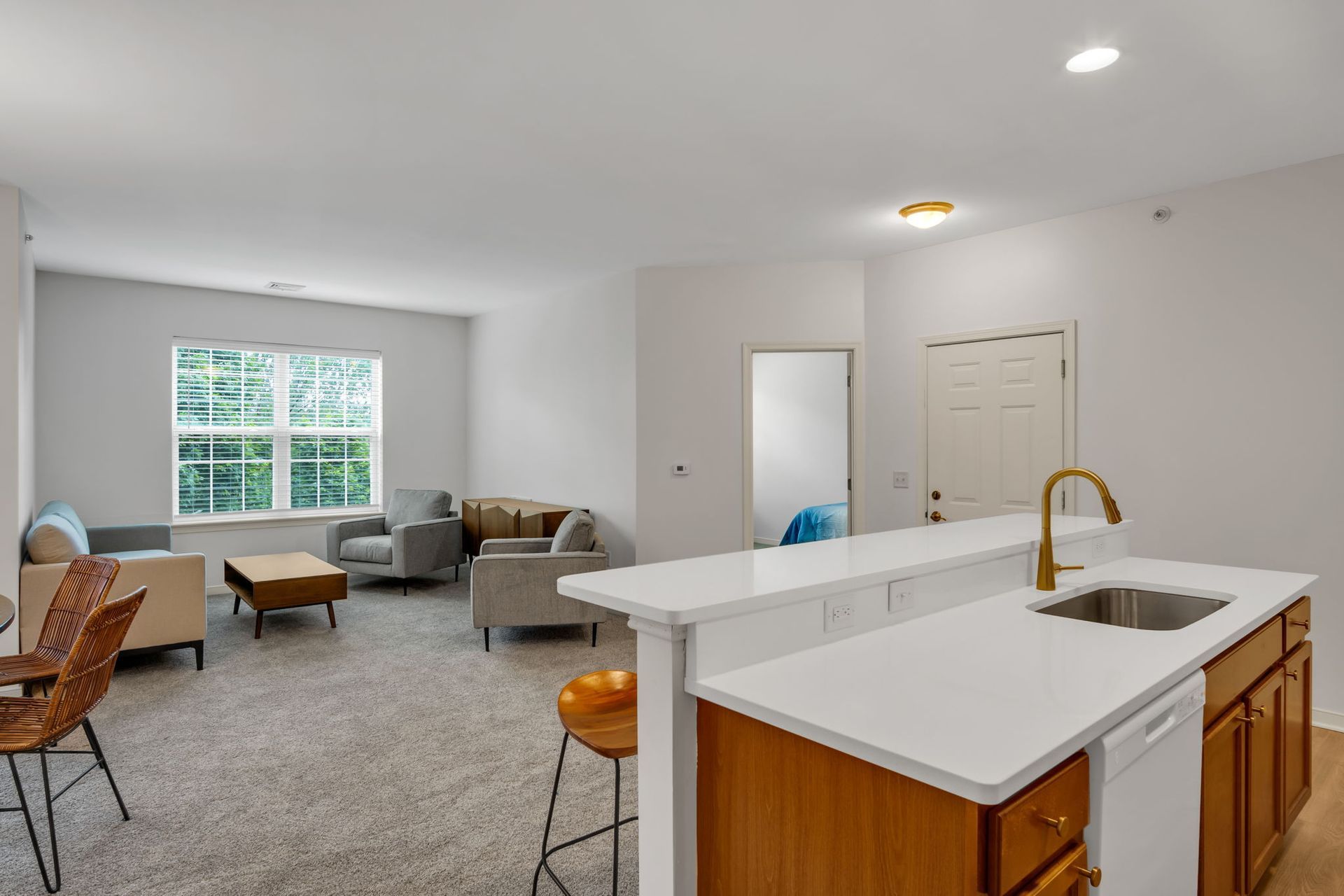 Bright open living room and kitchen with gray sofa, white island, wood cabinets, and large window