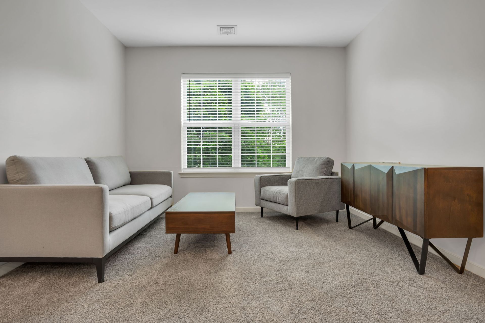 Bright living room with a gray sofa, armchair, coffee table, and wooden sideboard by a window.