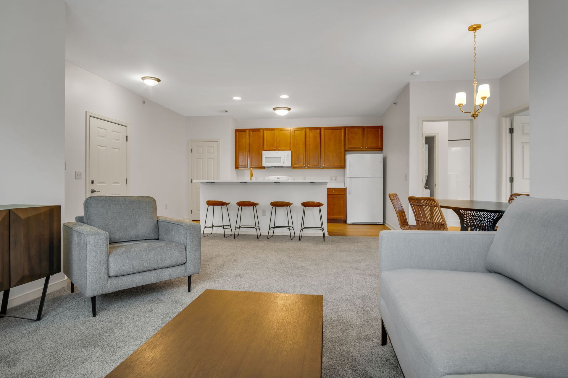 Bright living room with gray sofas, a wooden coffee table, and an open kitchen with bar stools.