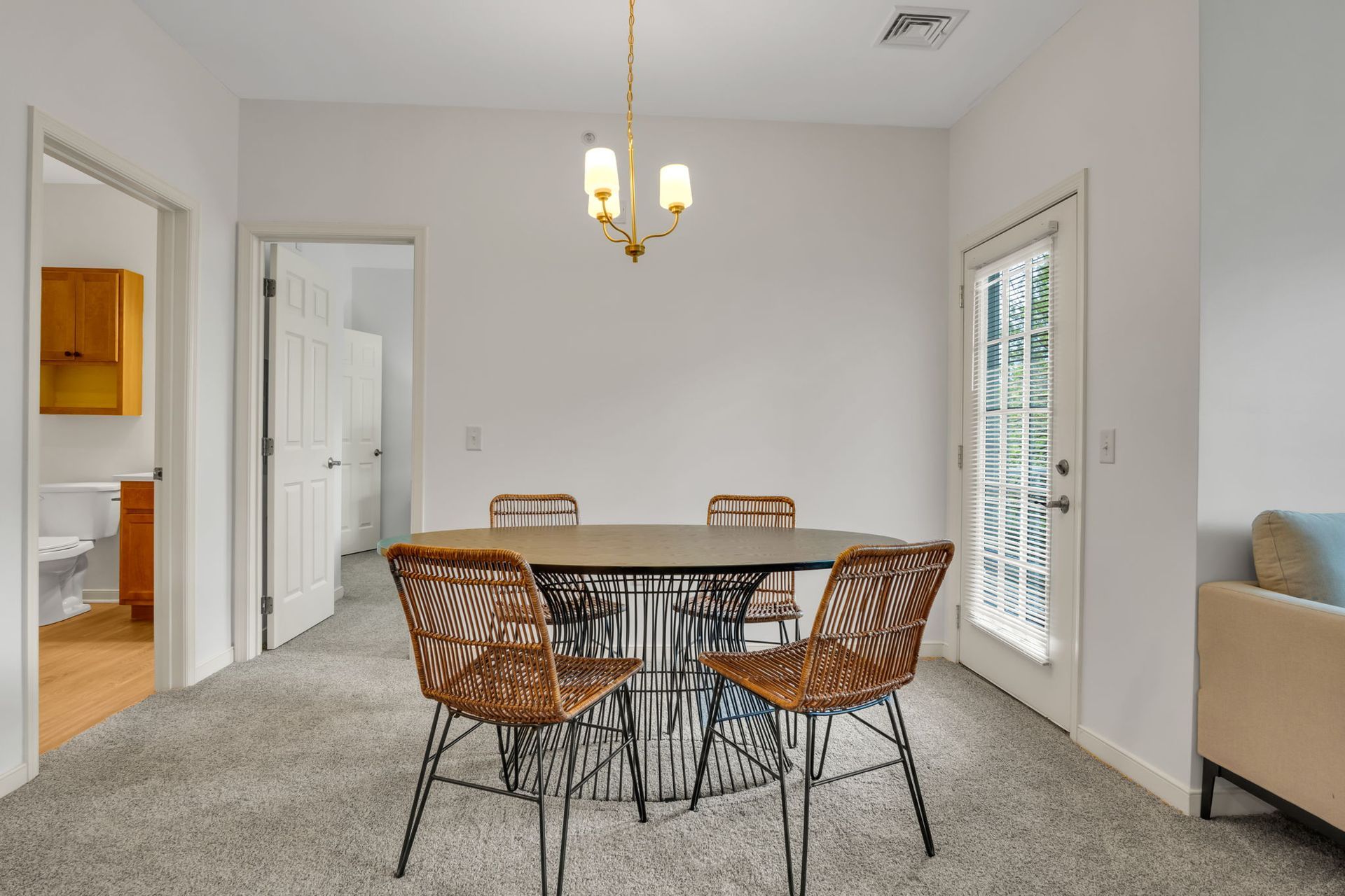 Dining room with a round wooden table, wicker chairs, chandelier, and white walls.