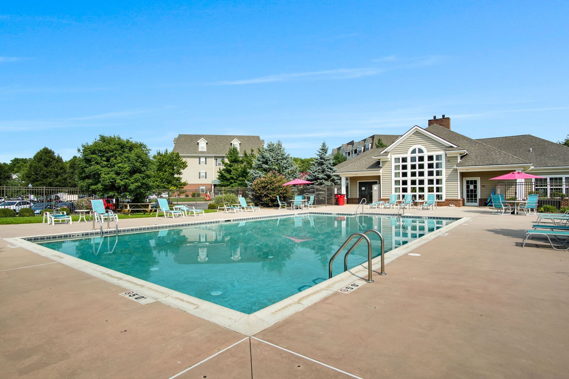 Outdoor swimming pool beside a clubhouse with lounge chairs and umbrellas under a clear blue sky