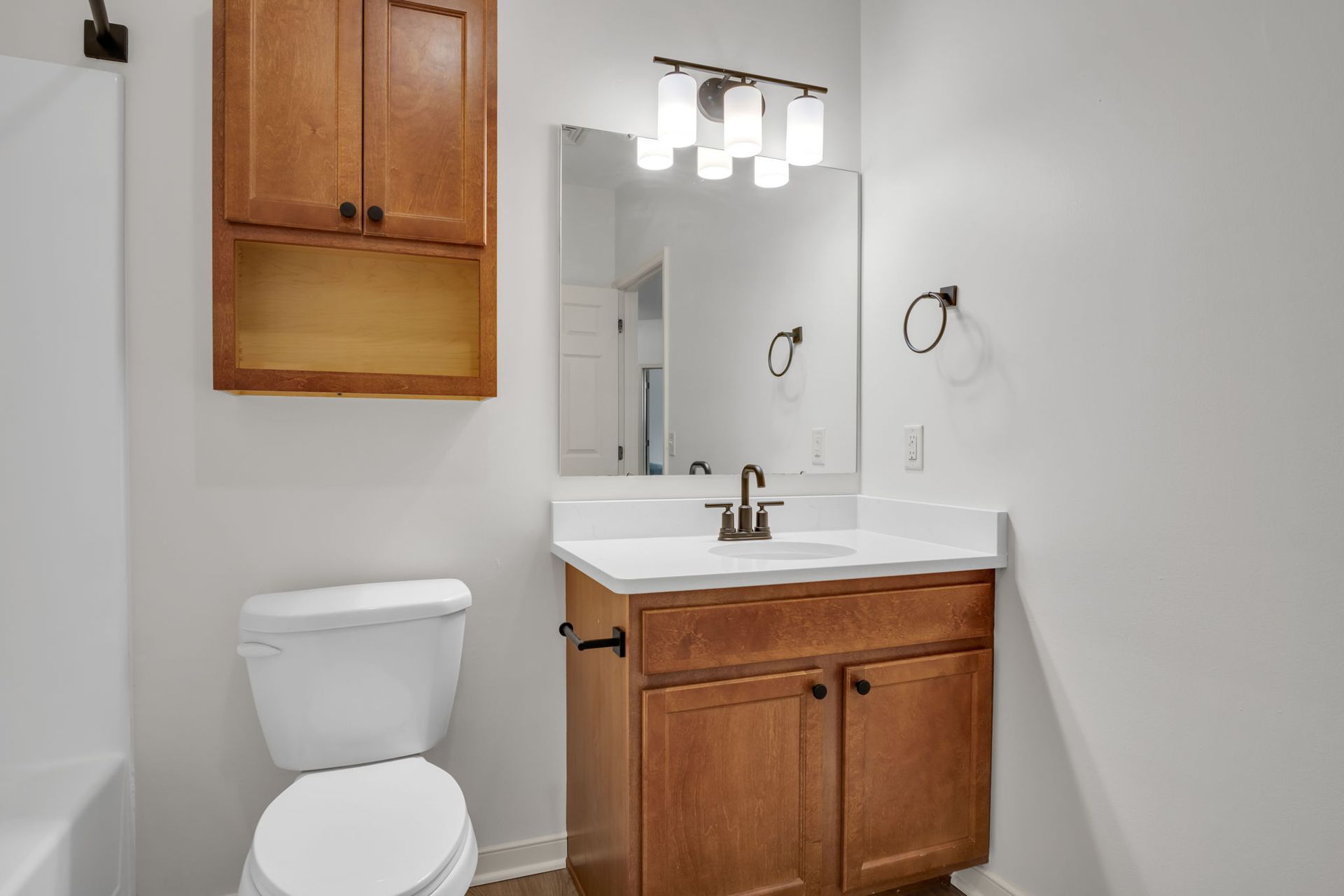 Small bathroom with wooden vanity, white toilet, mirror, and wall light fixtures
