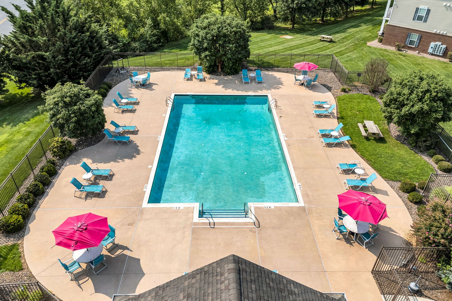Outdoor swimming pool with turquoise water, teal lounge chairs, and pink umbrellas on a sunny patio