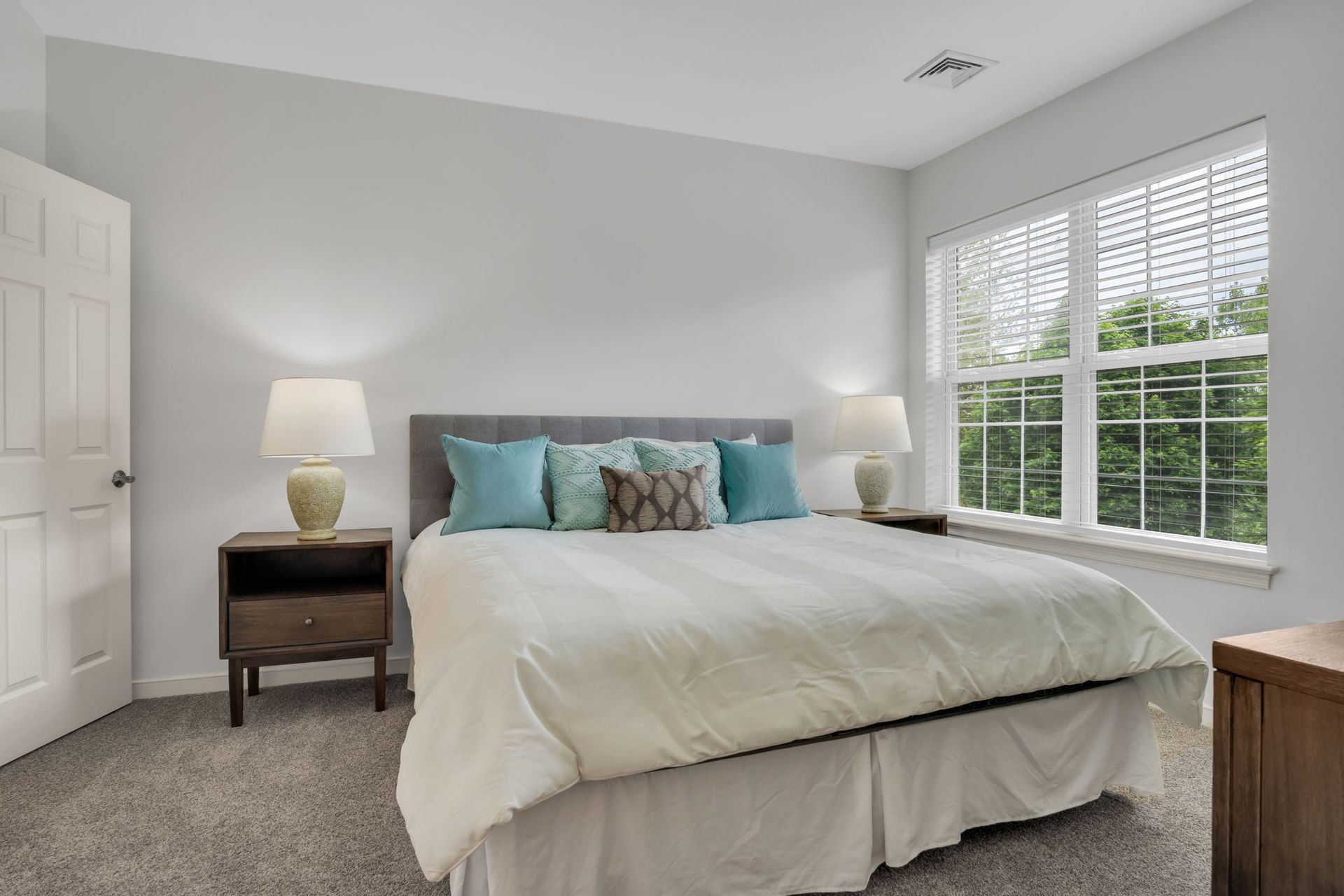 Bright bedroom with a large bed, two bedside lamps, and a window letting in natural light