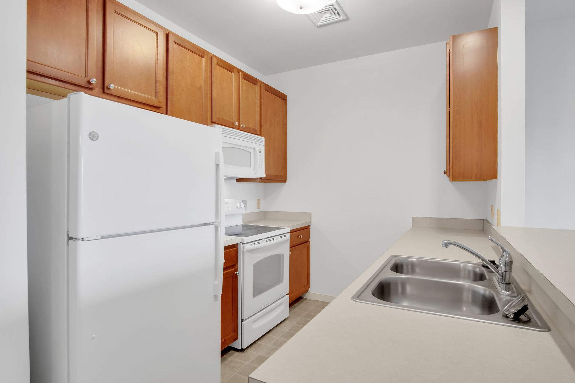 Small white kitchen with wood cabinets, white appliances, and a double sink with beige counters