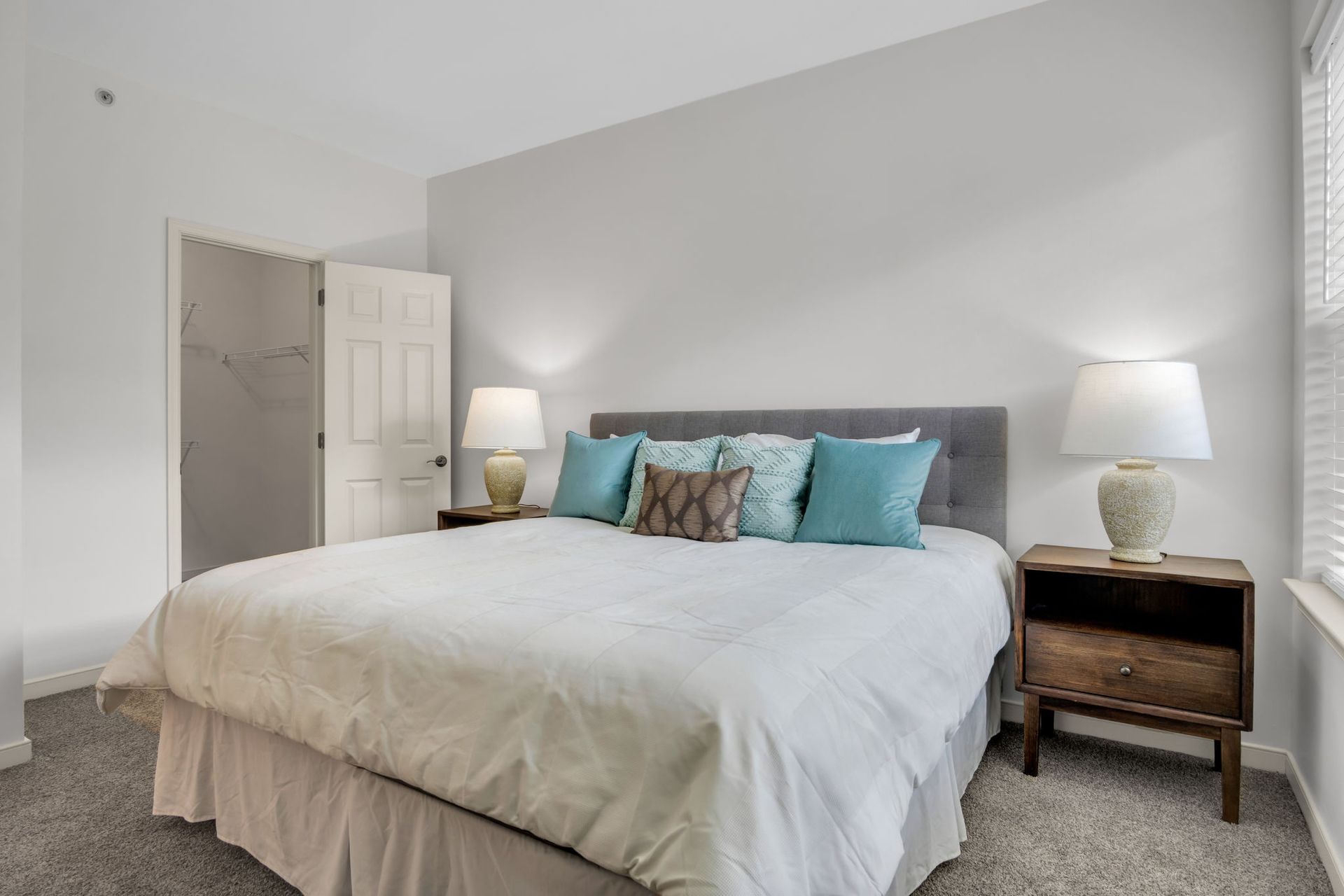 Bright bedroom with a white bed, gray headboard, teal pillows, and two bedside lamps.