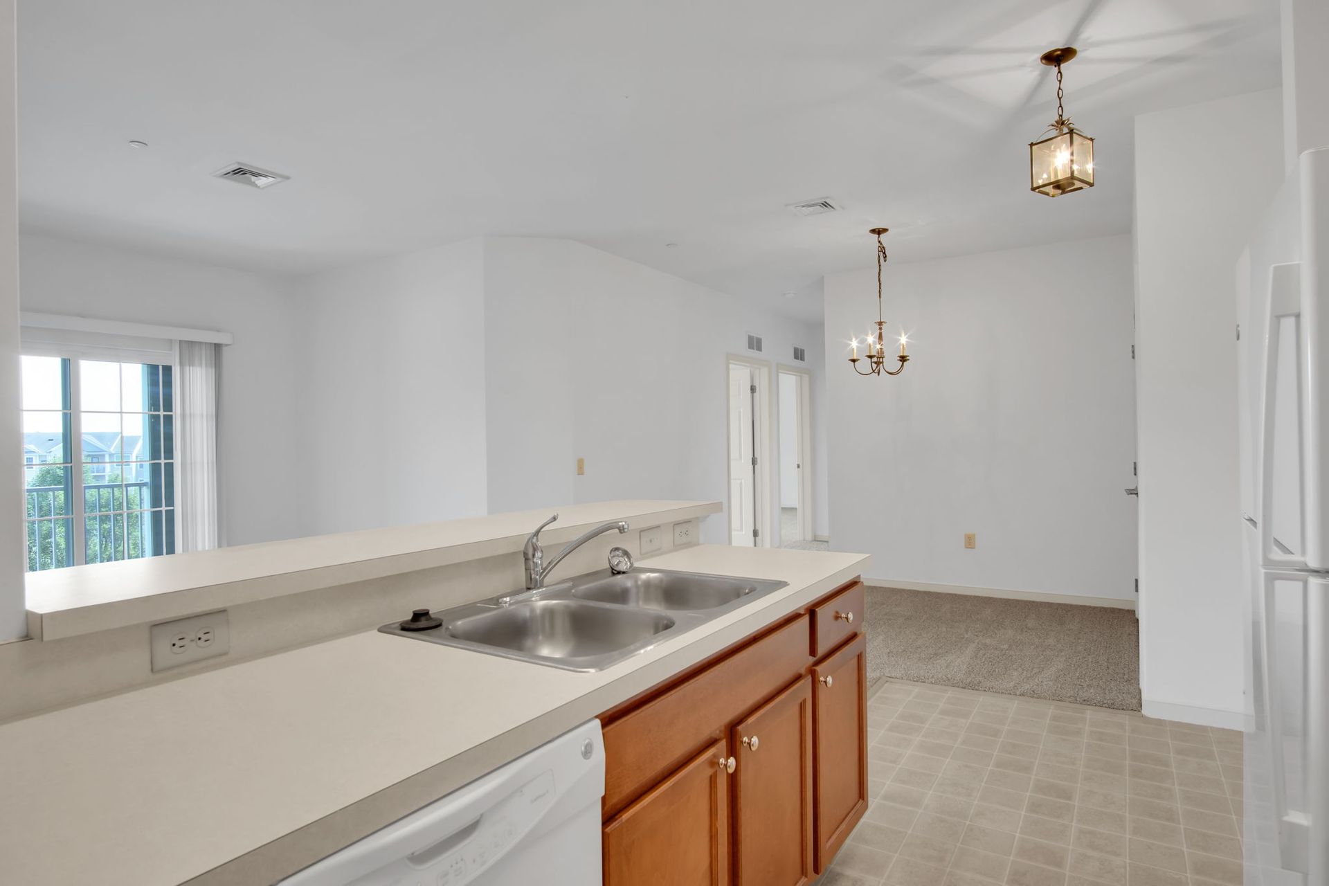 Bright empty kitchen with island sink, white walls, beige tile floor, and hanging pendant lights