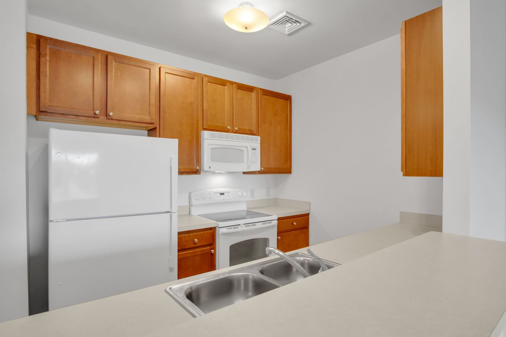 Small white kitchen with wood cabinets, white appliances, and a double sink at the counter.
