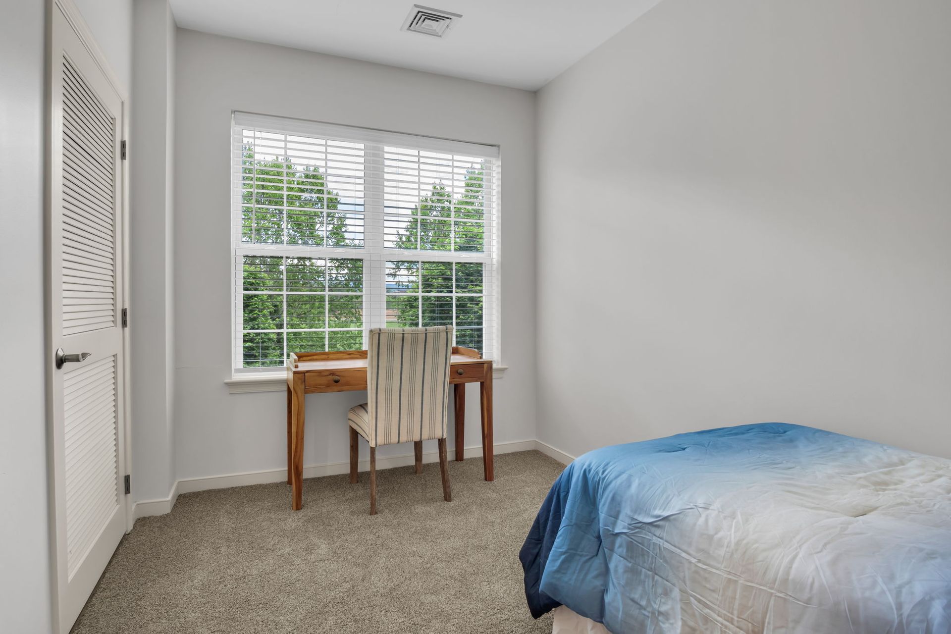 Small bedroom with a bed, desk, chair, and window with white blinds.