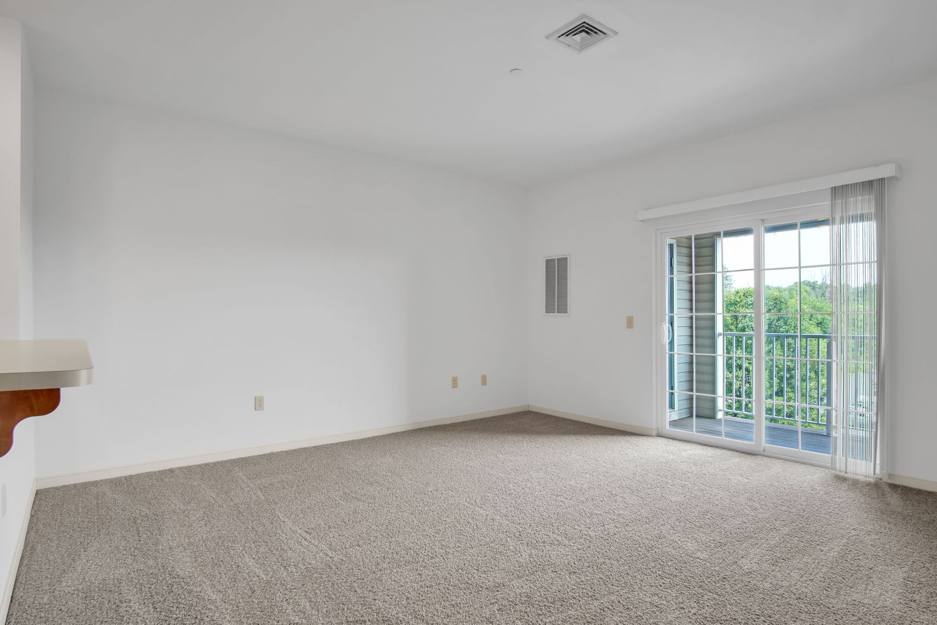 Empty carpeted living room with white walls and sliding glass doors opening to a balcony