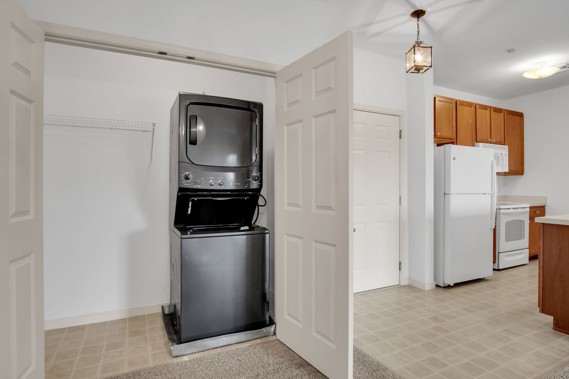 Empty laundry and kitchen area with stacked washer and dryer beside white closet doors