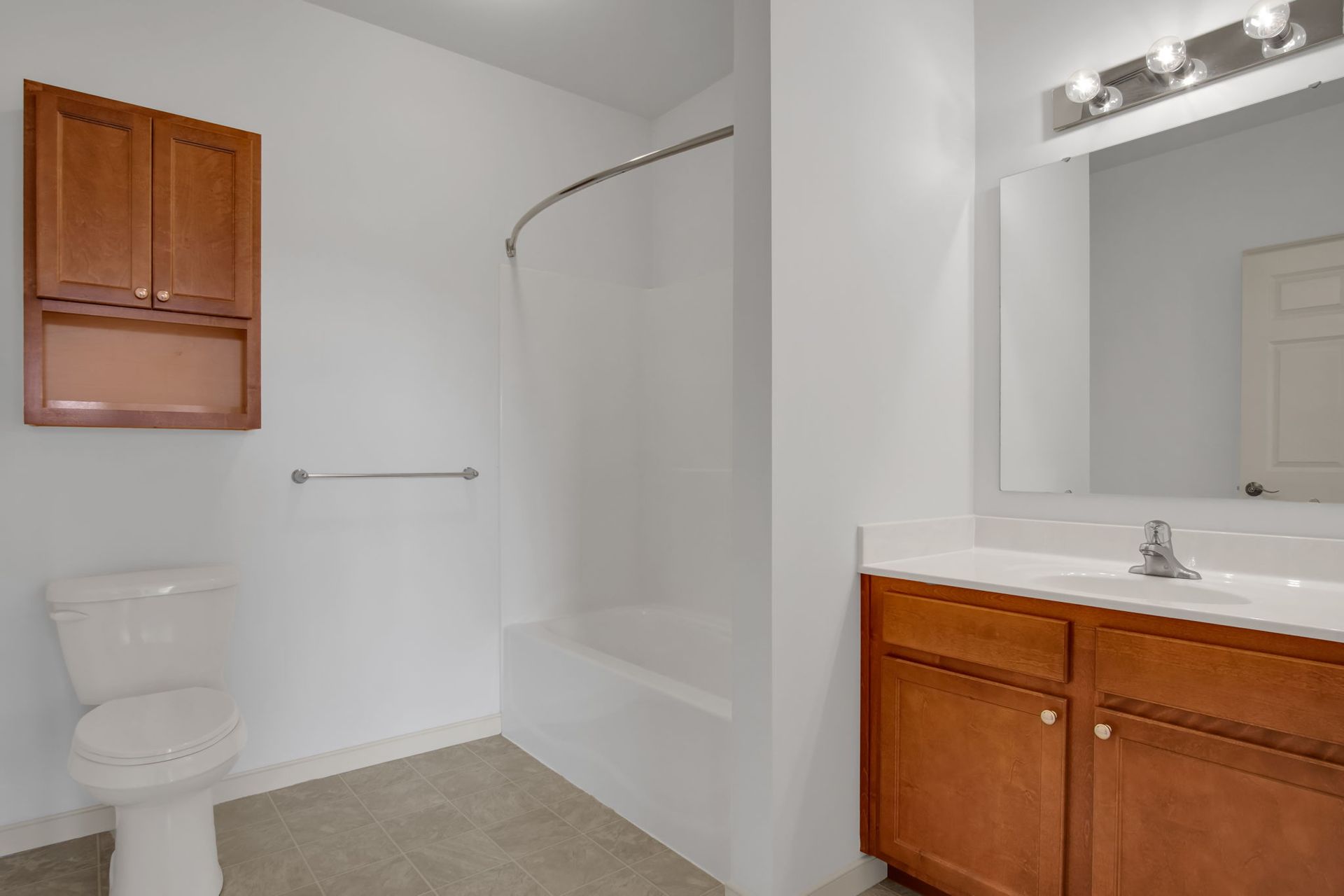 Small bathroom with toilet, bathtub, wooden vanity, and white walls.