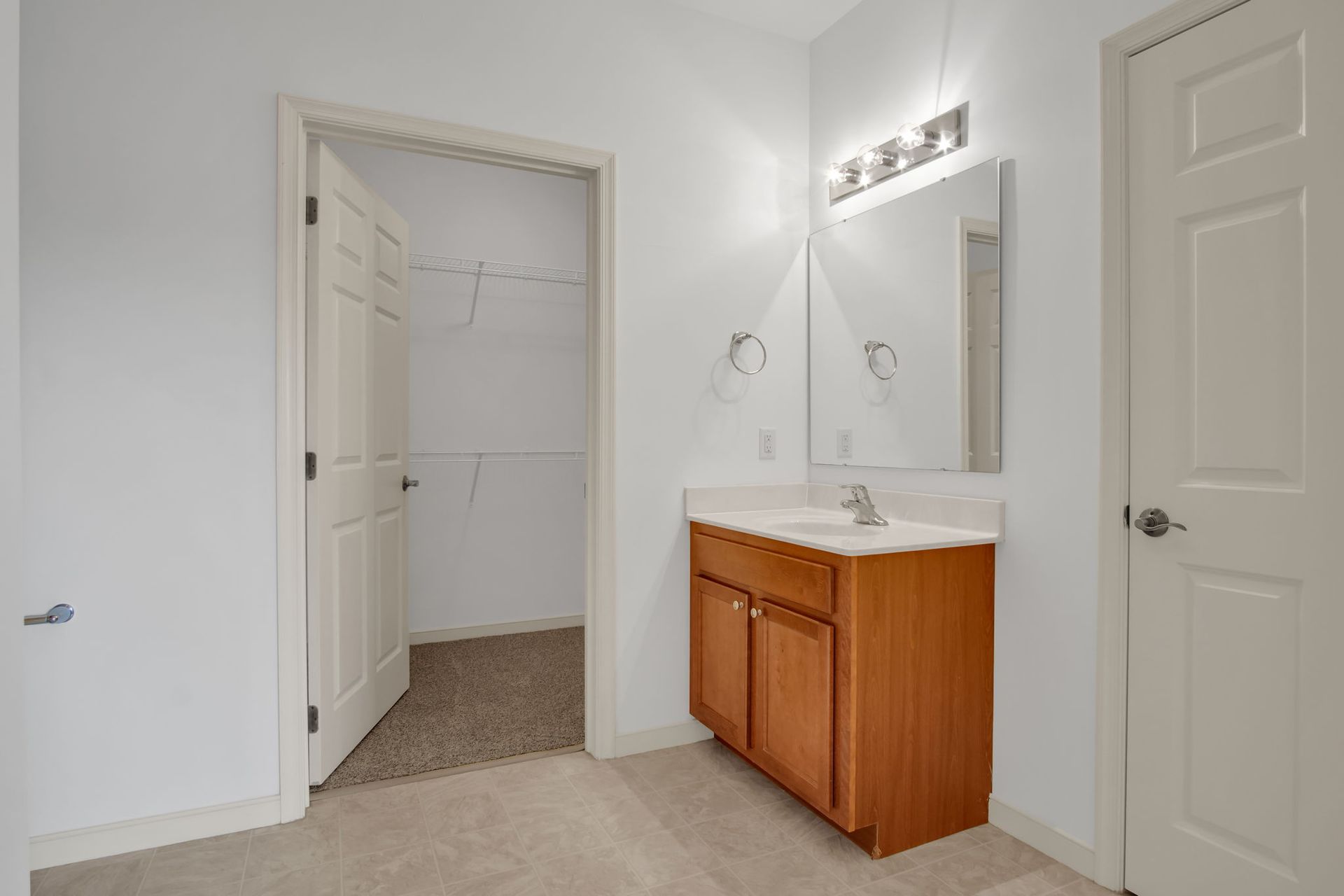Bathroom with white walls, vanity cabinet, mirror, and open closet doorway.