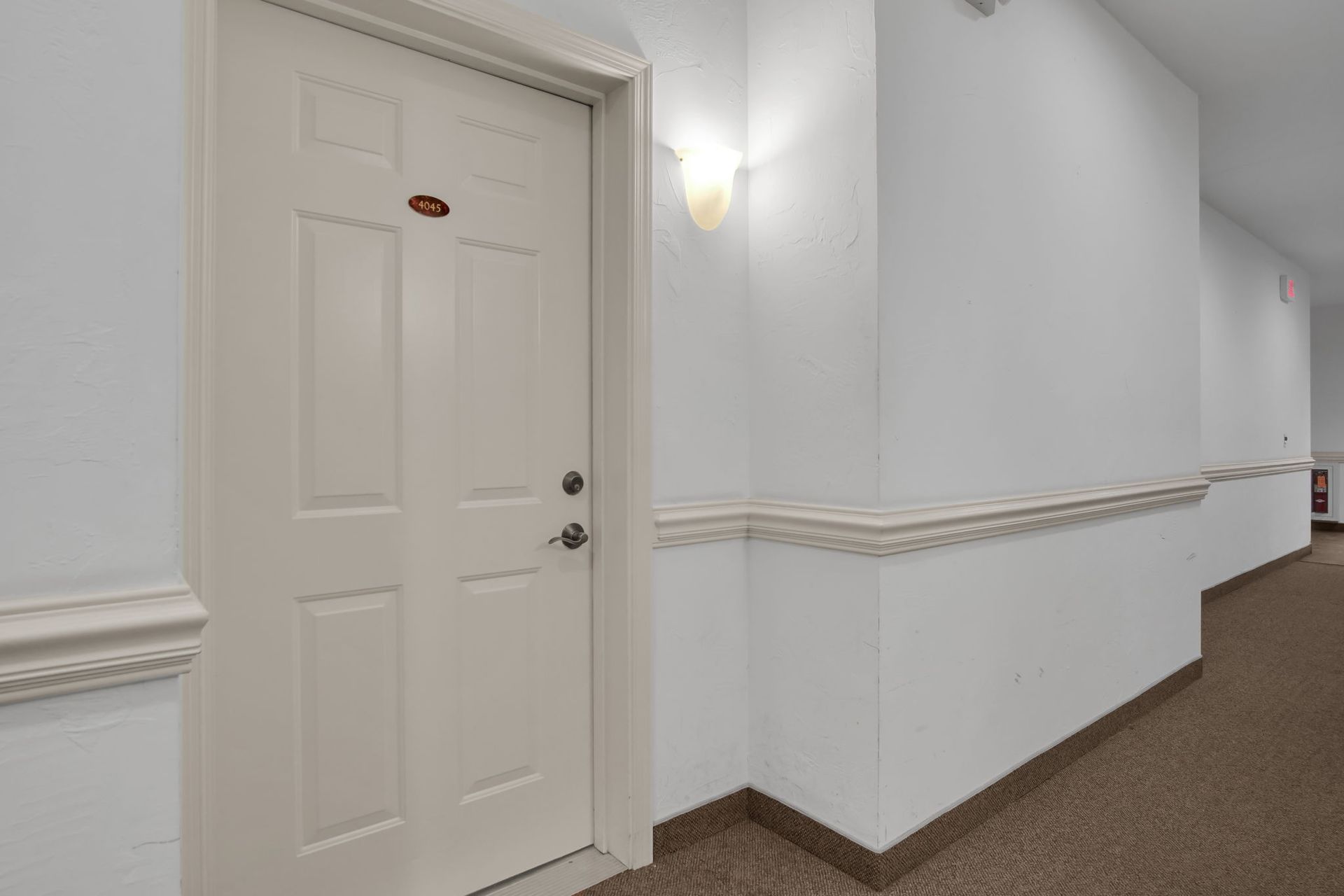 White hallway with a closed beige door and wall sconce on the left.