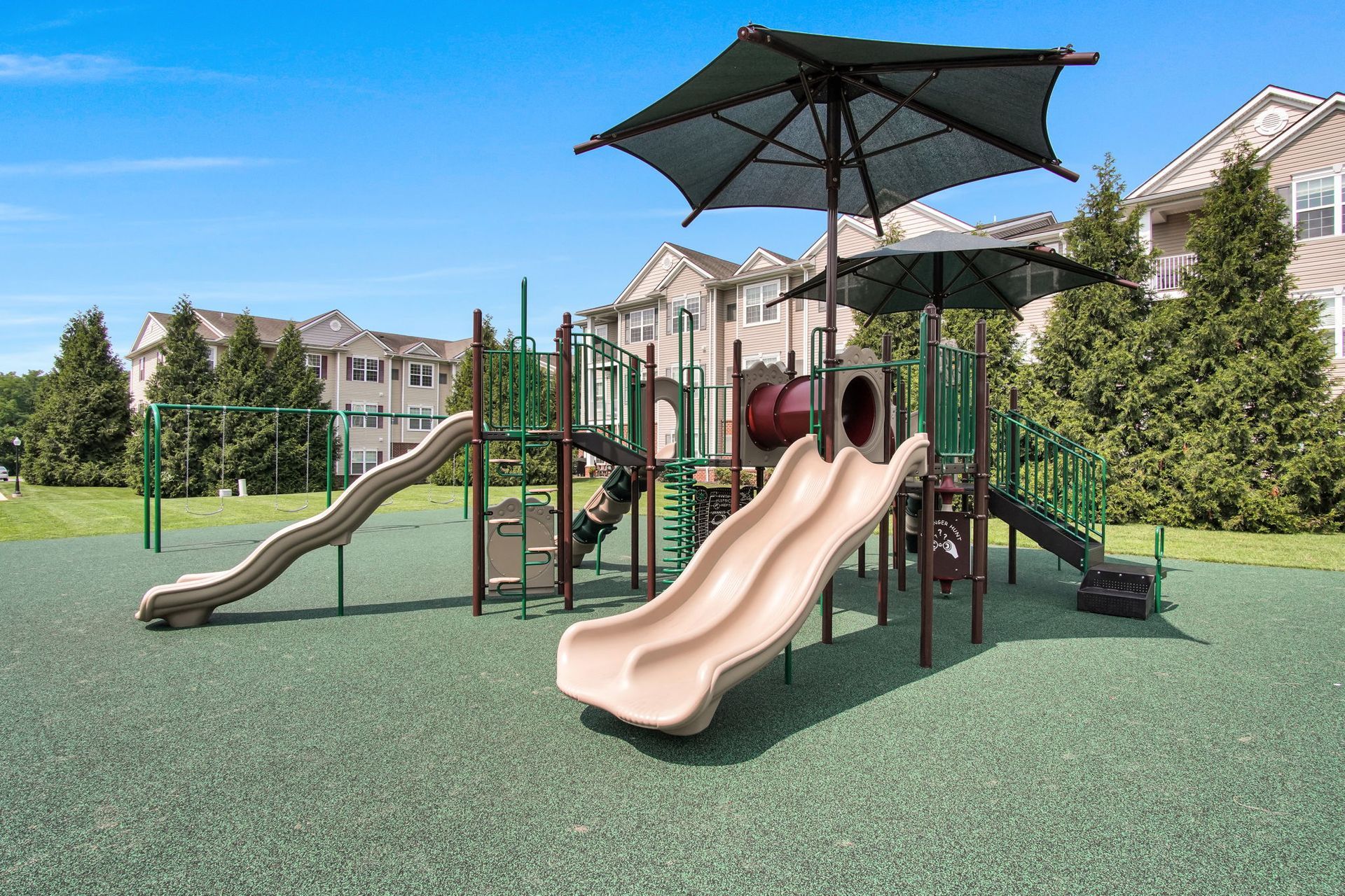 Children’s playground with slides and climbing structure on a green rubber surface under a shade canopy