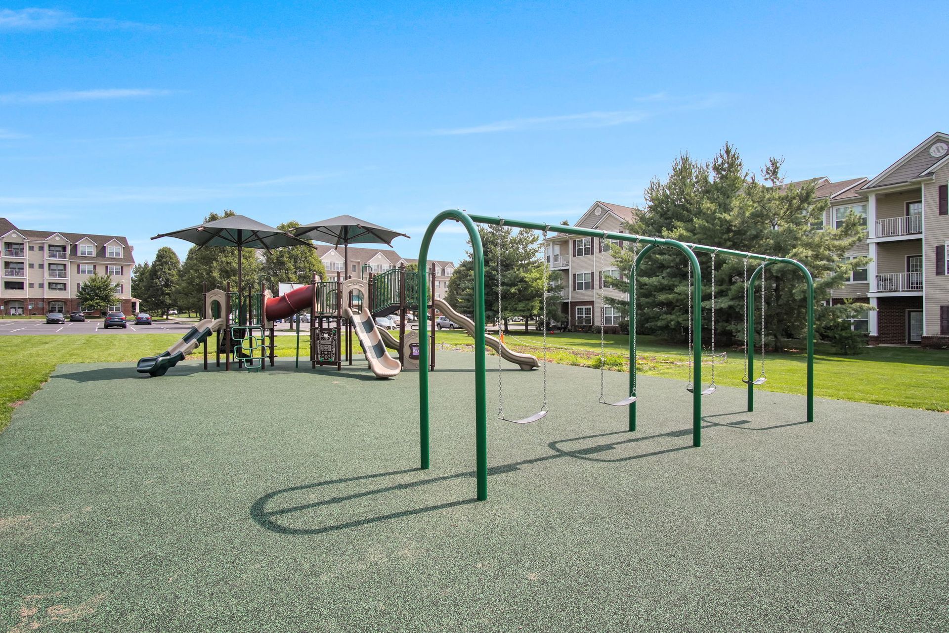Apartment courtyard playground with green climbing bars, slide, and swings on synthetic turf
