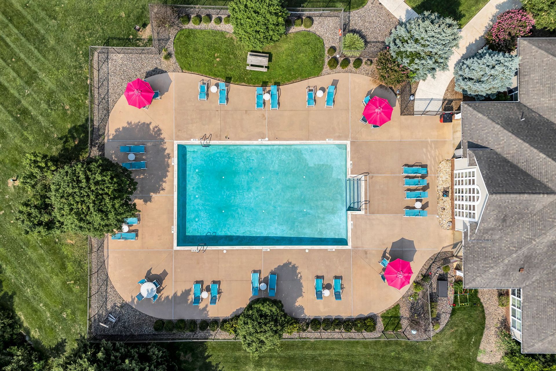 Overhead view of a backyard pool with lounge chairs, umbrellas, and patio seating on a sunny day