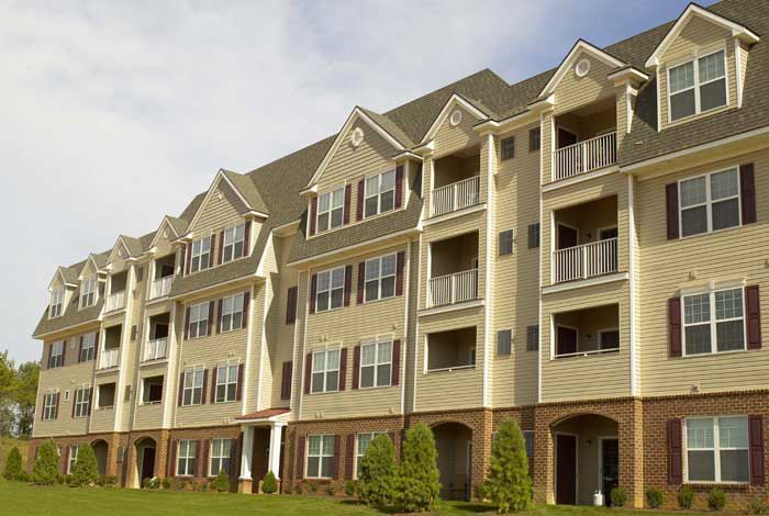 Three-story beige apartment building with balconies and dormer windows under a blue sky