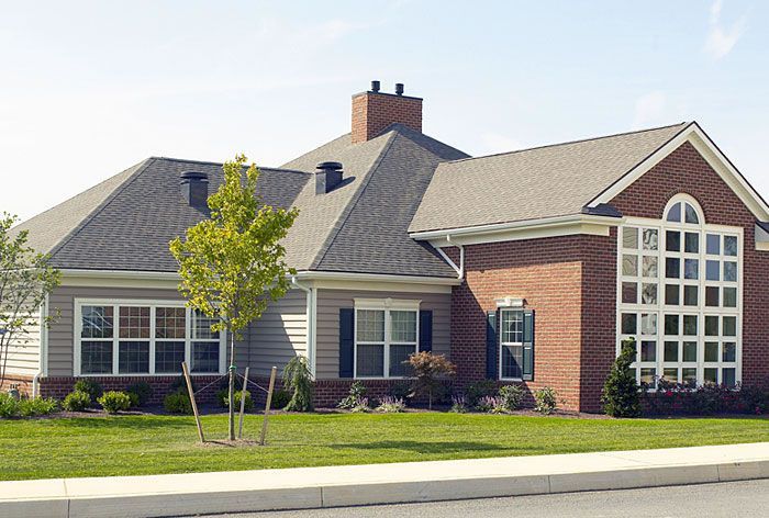 Single-story brick and siding house with large arched windows and a chimney on a sunny street
