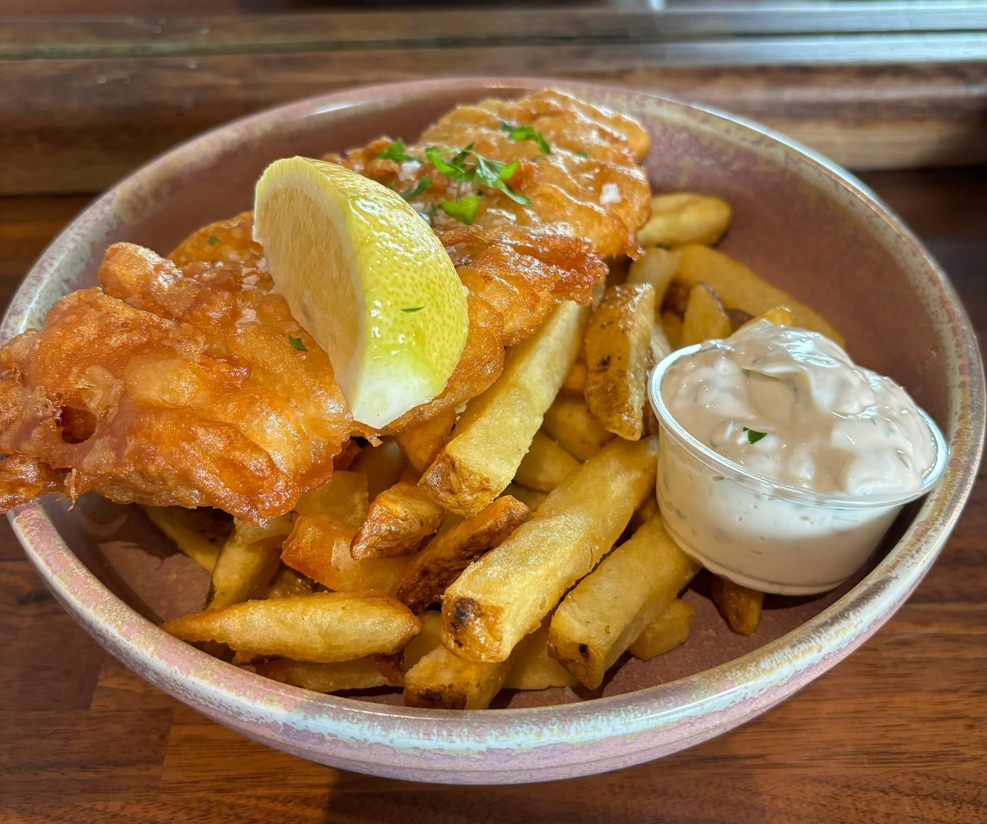 A bowl of fish and chips with a slice of lemon and dipping sauce.