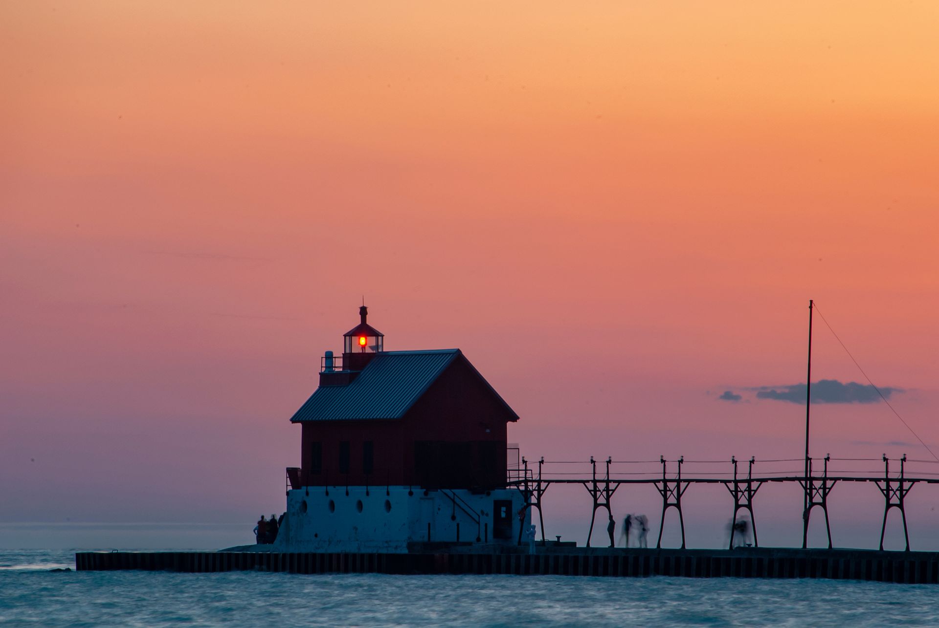 A lighthouse on a pier in the middle of the ocean at sunset.