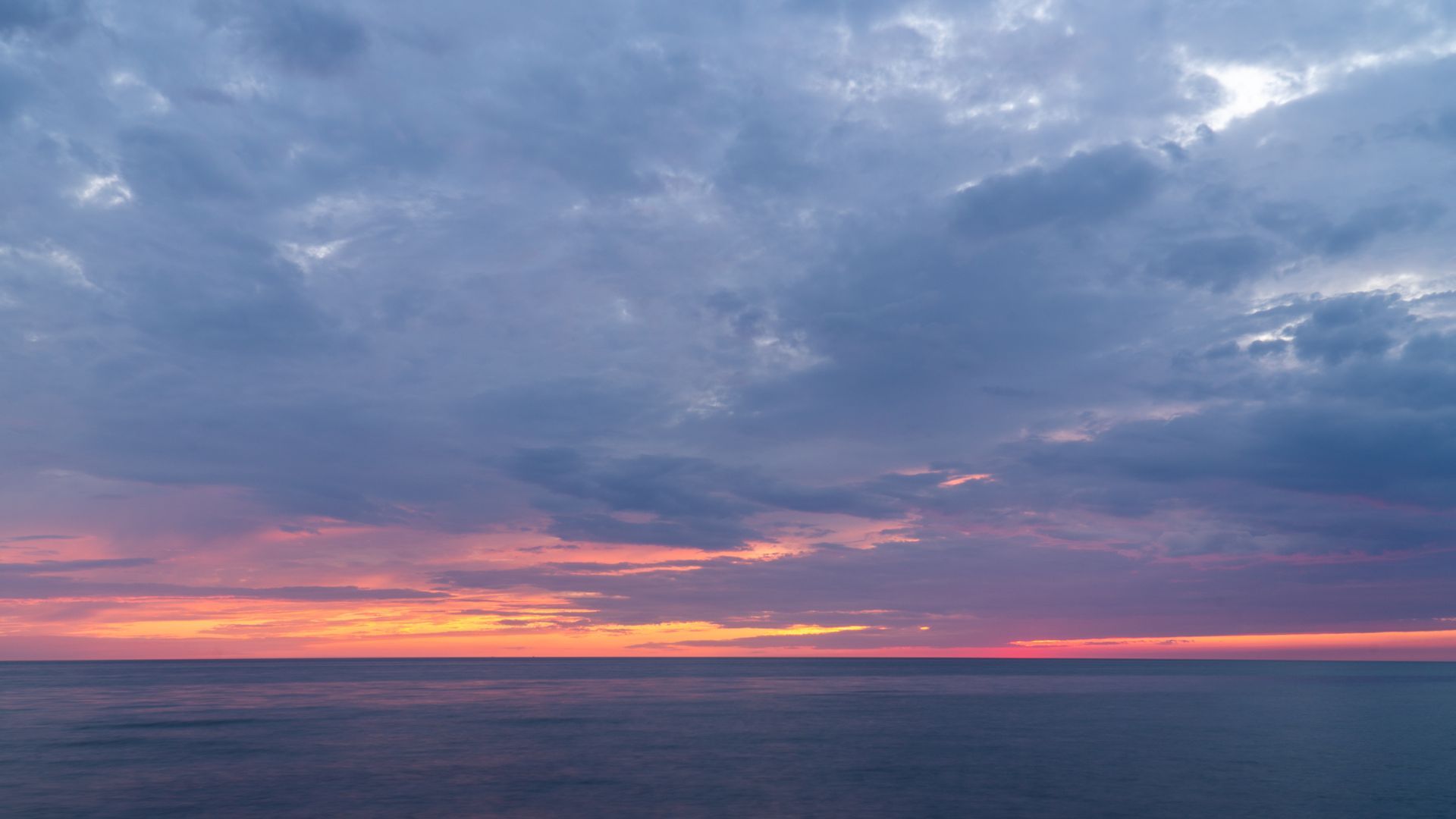 A sunset over the ocean with a cloudy sky