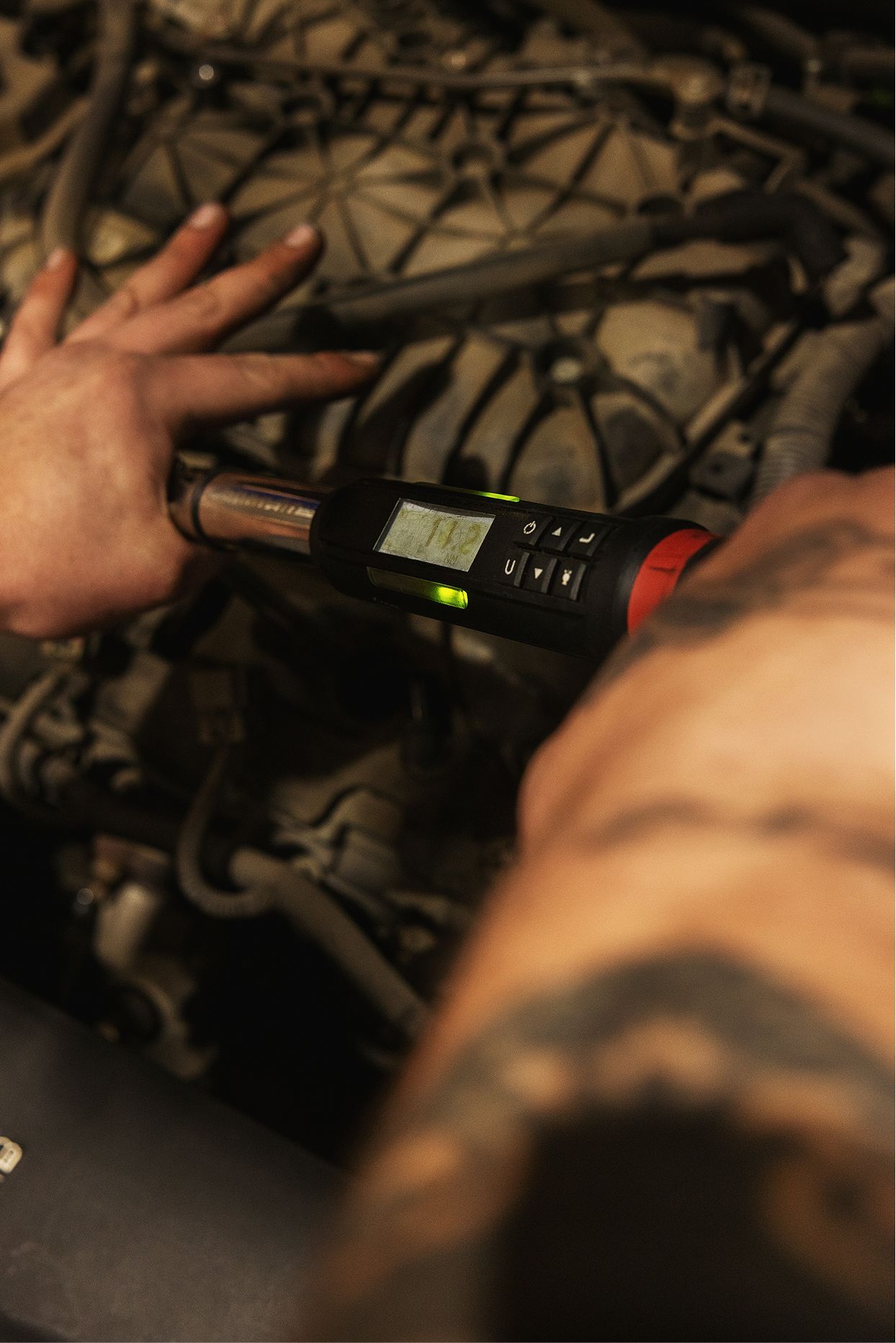 Person using a digital torque wrench on an engine, viewed from above, with tattoos on arm. | Gearhead Autoworks