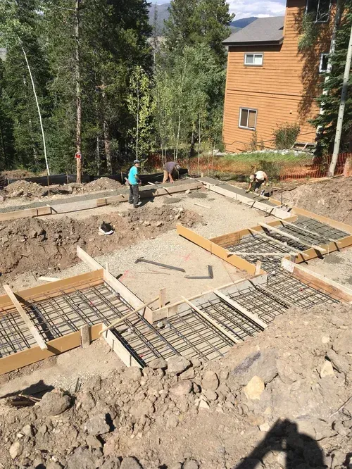 Foundation work with rebar and forms at a wooded construction site beside a cabin