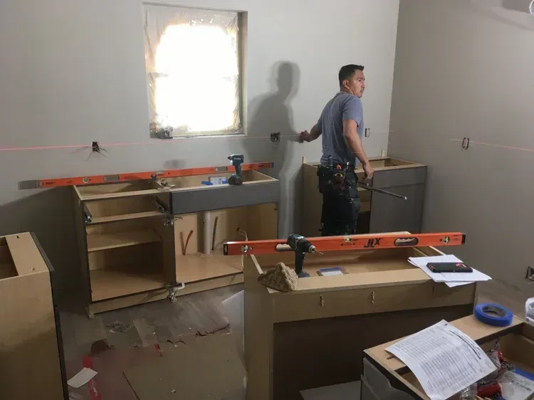 Person working in a room with cabinets, a window, and a level on a countertop during renovation.