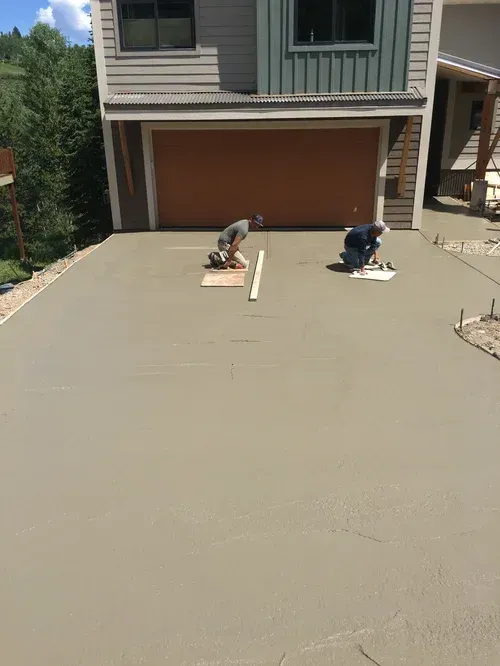 Two workers troweling a newly poured concrete driveway in front of a garage