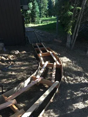 Curved wooden track under construction beside a building, with gravel and trees in the background