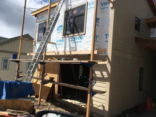 Two-story house under construction with scaffolding and a ladder against the exterior wall
